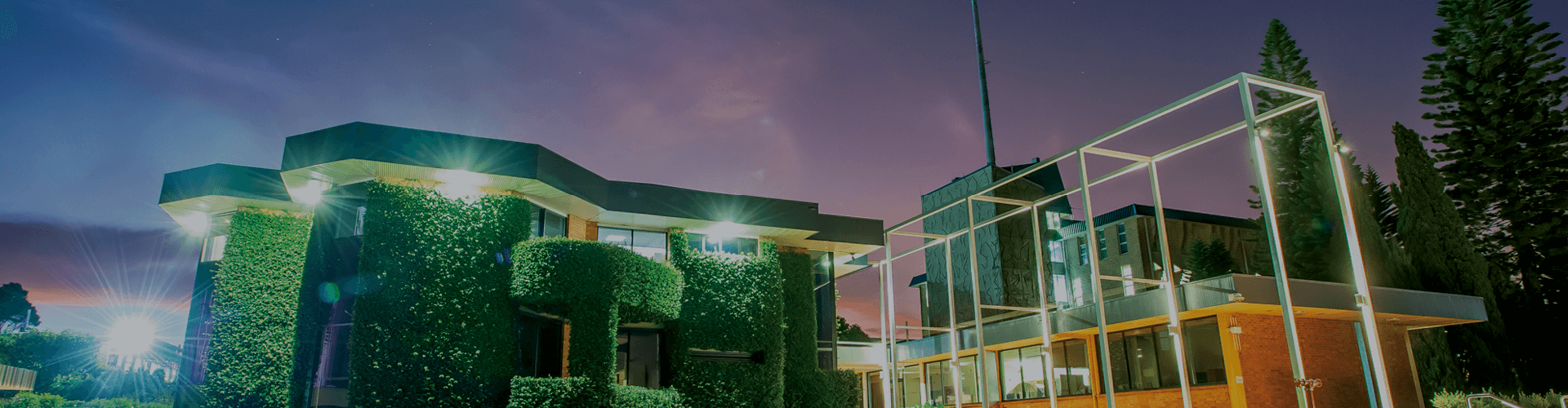 UniSQ Toowoomba illuminated at dusk with an artistic architectural design and surrounding greenery.