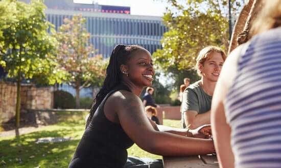Group of students interacting outdoors on a sunny campus setting.