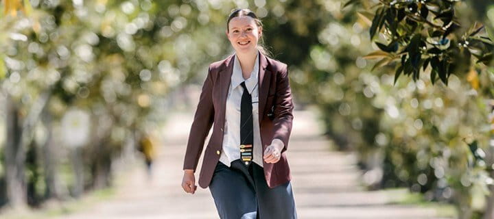 A woman in business attire smiling as she walks outdoors on a sunny day.